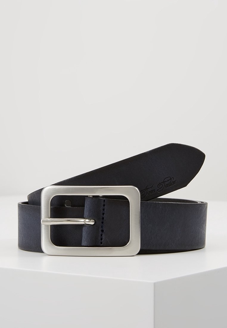 Ceinture en cuir noir avec une grande boucle rectangulaire argentée posée enroulée sur une surface blanche.