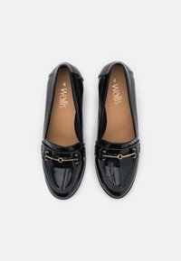 Černé lakované kožené mokasíny s hladkým povrchem, které mají zdobný zlatý kovový prvek přes přední část.