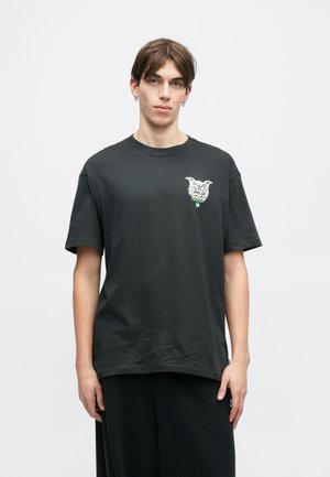 Crna pamučna majica s kratkim rukavima, sa šarenim grafičkim prikazom na prsima. Jednostavan dizajn s okruglim izrezom, širok kroj.