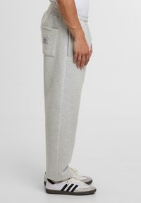 Hellgraue Sweatpants mit lockerem Schnitt, elastischem Bund, seitlichen Taschen und kleinem Logopatch. Kombiniert mit weißen und grauen Sneakers.