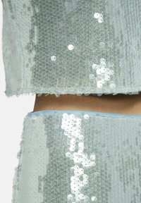 Lichtblauw paillettenstof met een textuurpatroon. Bevat opeenvolgende rijen glanzende witte pailletten op een gaasbasis, waardoor een glinsterend effect ontstaat.