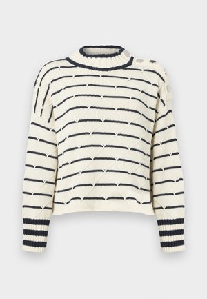 Kremasta pletena pulover s temno modrimi vodoravnimi črtami, visokim ovratnikom, rebrastimi manšetami in okrasnimi gumbi na enem ramenu. Teksturna vzorčena struktura skozi celotno oblačilo.