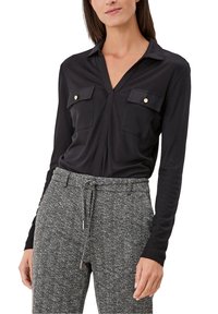 Blusa nera a maniche lunghe con scollatura a V, due tasche sul petto con bottoni dorati, abbinata a pantaloni a quadri grigio houndstooth.