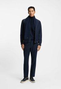 Giacca bomber della marina, dolcevita, pantaloni su misura e sneakers casual. Sciarpa con bordi frangiati. Tutti gli articoli in tonalità scure coordinate.