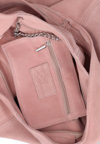 Interieur van een roze suède handtas met een ritsvak, kettinghengsel en gestikt rechthoekig merkembleem.