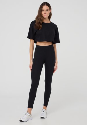 Maglietta nera a maniche corte e taglio corto abbinata a leggings neri a vita alta. Entrambi sono realizzati in un tessuto liscio e elasticizzato.