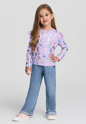 Maglietta a maniche lunghe lilla con spalle arricciate, caratterizzata da un motivo a stelle multicolore, abbinata a jeans in denim azzurro chiaro e sneakers in tonalità pastello.