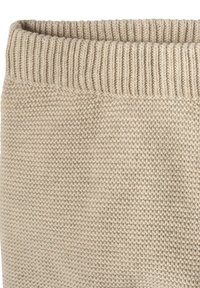 Beige gestrickter Stoff mit einem strukturierten Muster und einem gerippten Bündchen oben. Die Webart ist eng und gleichmäßig.