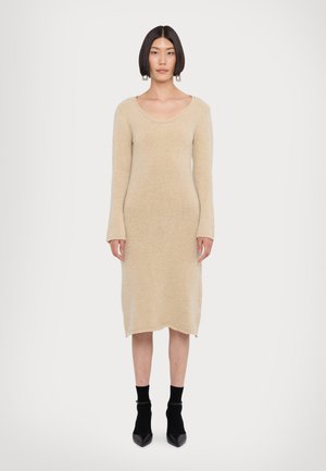 Beige lõngakootud kleit, millel on ümmargune kaelus, pikad varrukad ja kergelt kitsenev alläär. Kanda mustade pahkluu sokkide ja terava nina kingadega.