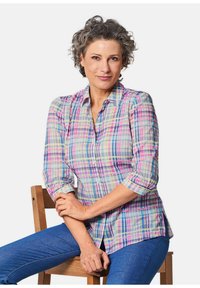 Camicia a quadri in colori pastello con blu, rosa, verde e giallo. Presenta un colletto classico e maniche a tre quarti, indossata con jeans blu.