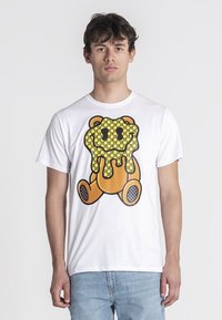 Camiseta de algodón blanca con un diseño de oso de dibujos animados y un patrón amarillo que gotea. Manga corta y cuello redondo.