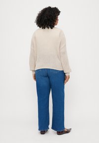 Bež pulover z pletenimi detajli in oversize rokavi, v kombinaciji z modrimi ravnimi kavbojkami in temno rjavimi balerinkami. Teksturovana tkanina in sproščen kroj.