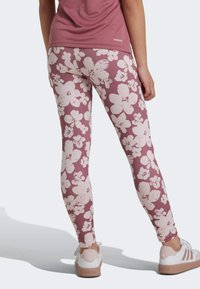 Leggings in deep mauve with white floral pattern; smooth texture, fitted design; paired with white and pink athletic shoes.