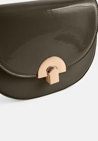 Bolso de mano de charol verde oscuro con un cierre de herrajes dorados en forma de semicírculo y costuras grises contrastantes a lo largo de los bordes. Textura lisa.