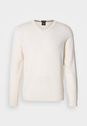 V-kaelusega kampsun heledas valges, valmistatud pehmest kudumkangast. Omab pikki varrukaid ja diskreetset logo tikandit vasakul rinnal.