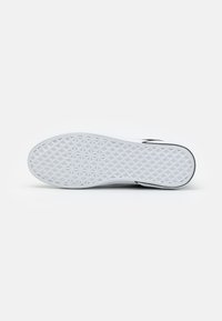 Suela de zapatilla blanca con una superficie texturizada y patrón, que presenta un diseño geométrico para mayor tracción. Contorno negro cerca del borde superior.