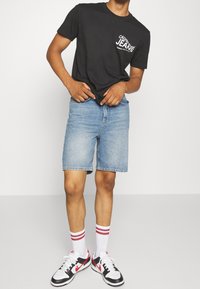 Black cotton t-shirt with white branding, blue denim shorts, red-striped white socks, and black, white, and red sneakers.