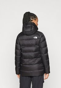 Casaco puffer preto com capuz, design acolchoado e logótipo na parte de trás superior. Acabado com uma textura suave e brilhante e punhos elásticos.