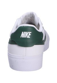 Zapatilla Nike blanca con detalle de talón de cuero verde, suela de goma texturizada, cuello acolchado y con un prominente logo blanco en la parte trasera.