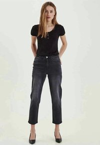 Mørk vasket denimjeans med slim fit, høy midje, fem lommer og glidelås. Kombinert med en tettsittende svart ribbestrikket topp og svarte hæler.