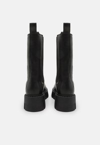 Bottes de cheville en cuir noir avec un design structuré, dotées d'une semelle en caoutchouc épaisse et de languettes à l'arrière pour un enfilage facile.