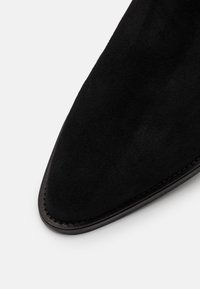 Stivale alla caviglia in suede nero con punta appuntita e suola in pelle nera cucita. Texture liscia senza motivi visibili o ferramenta.