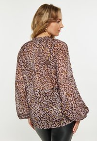 Blusa in stampa animale trasparente nei toni del rosa e marrone, con scollatura arricciata, maniche lunghe a sbuffo e un design fluido.
