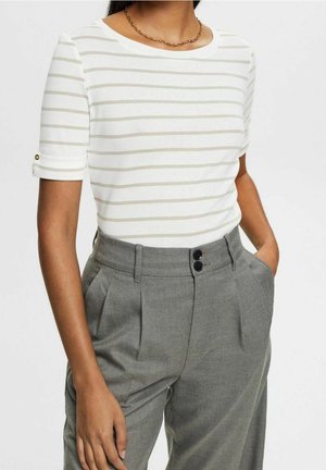 Witte top met korte mouwen en lichte grijze horizontale strepen, met opgerolde mouwboorden en gouden knopen; gecombineerd met hoog getailleerde, grijze, op maat gemaakte broek.