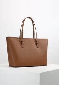 Sac fourre-tout en cuir synthétique marron avec une texture lisse, de forme rectangulaire, double anses et accents en métal doré.