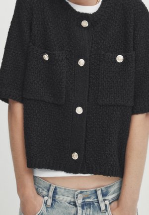 Czarny dzianinowy kardigan z krótkimi rękawami, posiadający dwie przednie kieszenie, duże srebrne guziki oraz fakturowany wzór. Krótki krój.
