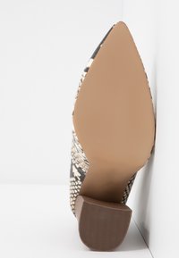 Chaussure à bout pointu avec un motif en peau de serpent noir et beige, une semelle brune lisse et un petit talon carré. Surface supérieure texturée.