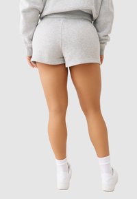 Szare szorty z mieszanki bawełny o miękkiej teksturze, z elastycznym paskiem w talii i zaokrąglonym końcem, w połączeniu z białymi sneakersami i skarpetkami sięgającymi do kostek.