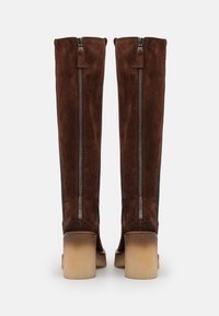 Botas de ante marrón hasta la rodilla con cremalleras laterales dobles, un tacón cuadrado y detalles texturizados a lo largo de los costados.