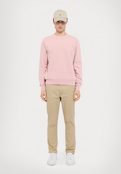 Lys rosa genser, beige caps, beige bukser og hvite sneakers. Enkelt design med ribbestrikkede manchetter og lite logo på brystet.