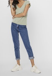 Ljusgrön t-shirt med v-ringning och rullade ärmar, parat med blå, avsmalnande denimjeans som är uppvikta vid anklarna, och vita sneakers.