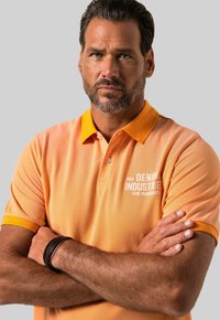 Polo tričko s krátkým rukávem v gradientní oranžové barvě s kontrastním žlutým límcem. Má vyšívané logo na hrudi a texturovanou tkaninu.