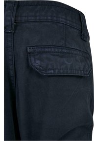 Mørkeblå denimjeans med en baklomme med formet klaff, strukturert stoff og synlig søm langs kantene.