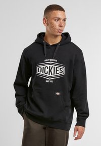Black sweatshirt with hood, featuring a large white "DICKIES" logo, kangaroo pocket, and ribbed cuffs. Made of soft fabric.