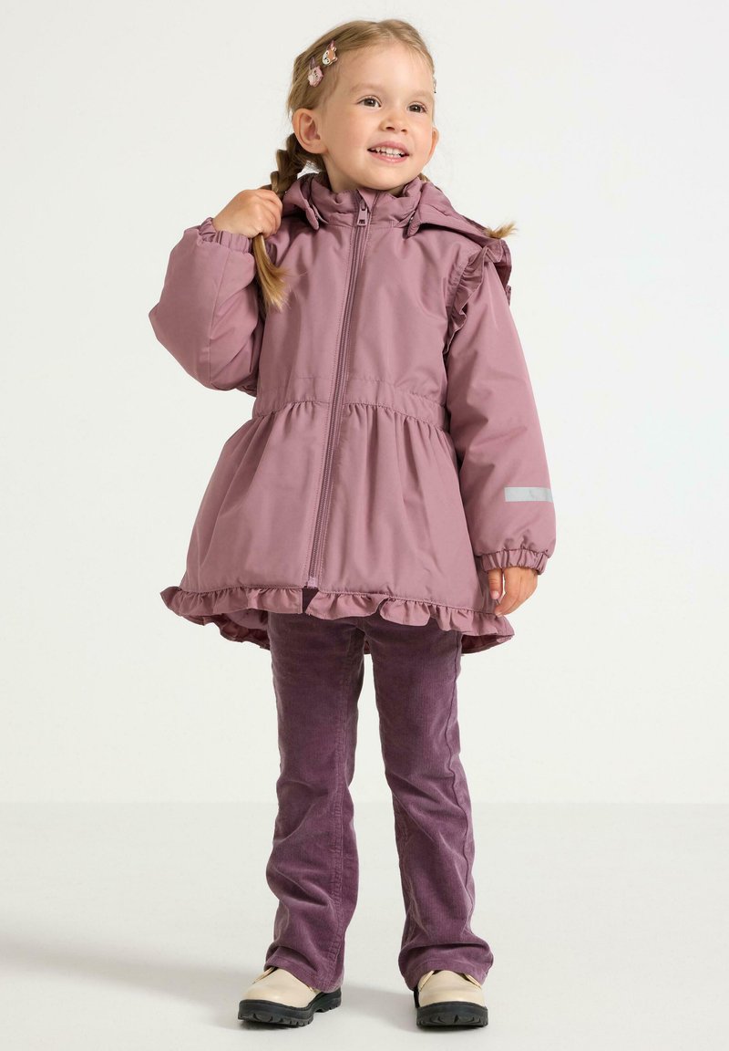 Roze gewatteerde jas met ruffle-onderkant en elastische manchetten, gecombineerd met paarse ribcordbroeken en schoenen met zwarte zolen.