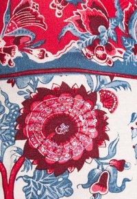 Tissu floral avec un motif rouge et bleu présentant une grande fleur rouge ornée de sequins, des feuilles contournées et des détails bleus raffinés.