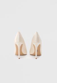 Μπεζ ψηλοτάκουνα γόβα με μυτερή μύτη, λεία υφή και λεπτό τακούνι στιλέτο. Διαθέτουν μινιμαλιστικό σχεδιασμό και διακριτικές ραφές.