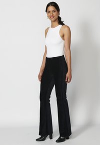 Witte mouwloze bodysuit in combinatie met hoge zwarte flared broeken, gemaakt van een gestructureerd materiaal, aangevuld met zwarte haklaarzen.
