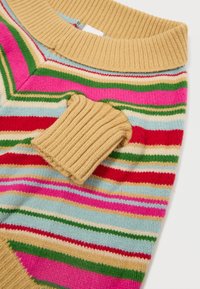 Sokszínű pulóver vízszintes csíkokkal rózsaszín, piros, zöld, kék és bézs színben. Bézs színű, bordás gallérja van, valamint egy textúrált, világosbarna folt.