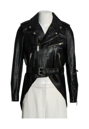 Chaqueta de motorista de piel negra con cremallera frontal asimétrica, múltiples bolsillos con cremallera, cinturón en la cintura y mangas largas sobre pantalones blancos.