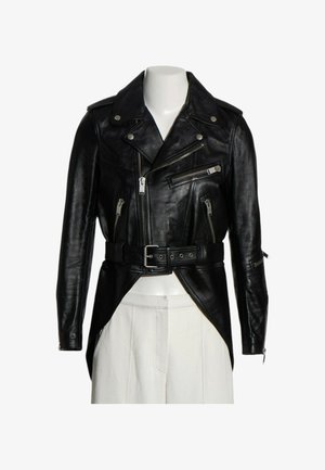 Zwarte leren motorjas met asymmetrische voorrits, meerdere zakken met rits, riem in de taille en lange mouwen over een witte broek.