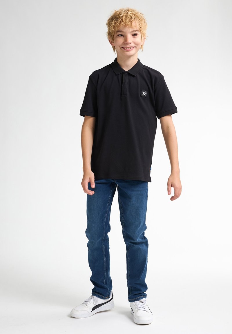 Svart polo med kort ärm och rund krage, tillsammans med blå jeans och vita sneakers. Har en liten logotyp på bröstet.