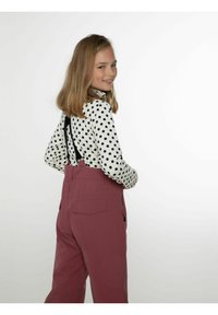 Valkoinen pitkähihaisellinen paita, jossa on mustia pilkkuja, yhdistetty pinkkeihin haalarikamppeisiin, joissa on säädettävät mustat hihnat ja sivutaskut vetoketjulla.