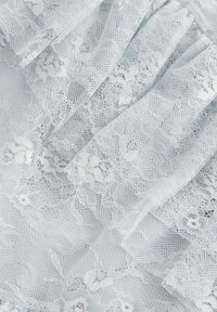 Tissu en dentelle bleu clair avec des motifs floraux, présentant des textures délicates et des couches qui créent de la profondeur et de la douceur.