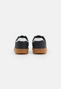 Black and white sneaker with a smooth upper, rear accents, and brown rubber sole. Features minimal branding and a low-profile design.