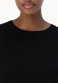 Black ribbed knit sweater with a round neckline. Smooth texture, close-fitting design, minimal seams, and no visible patterns or hardware.